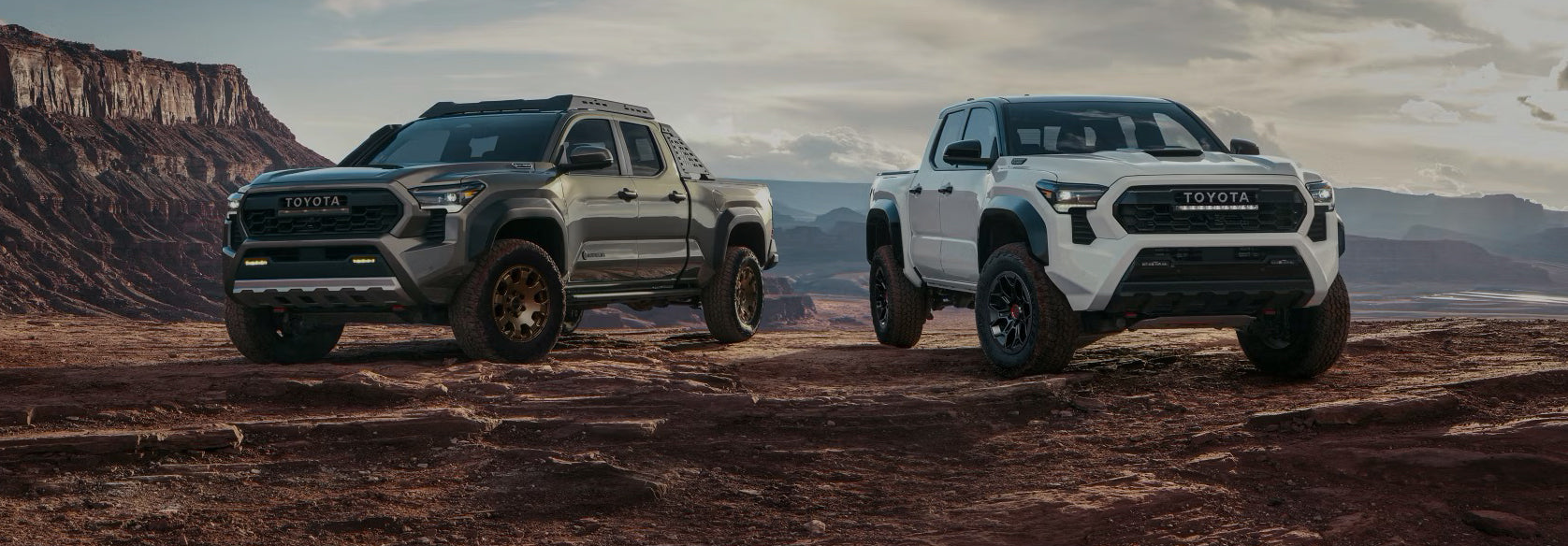 Two Toyota trucks on a desert landscape with mountains in the background