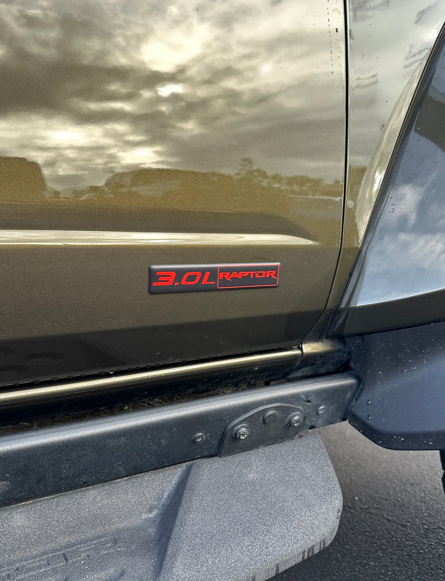 Close-up of a vehicle with a '3.0L Raptor' badge on a reflective surface.