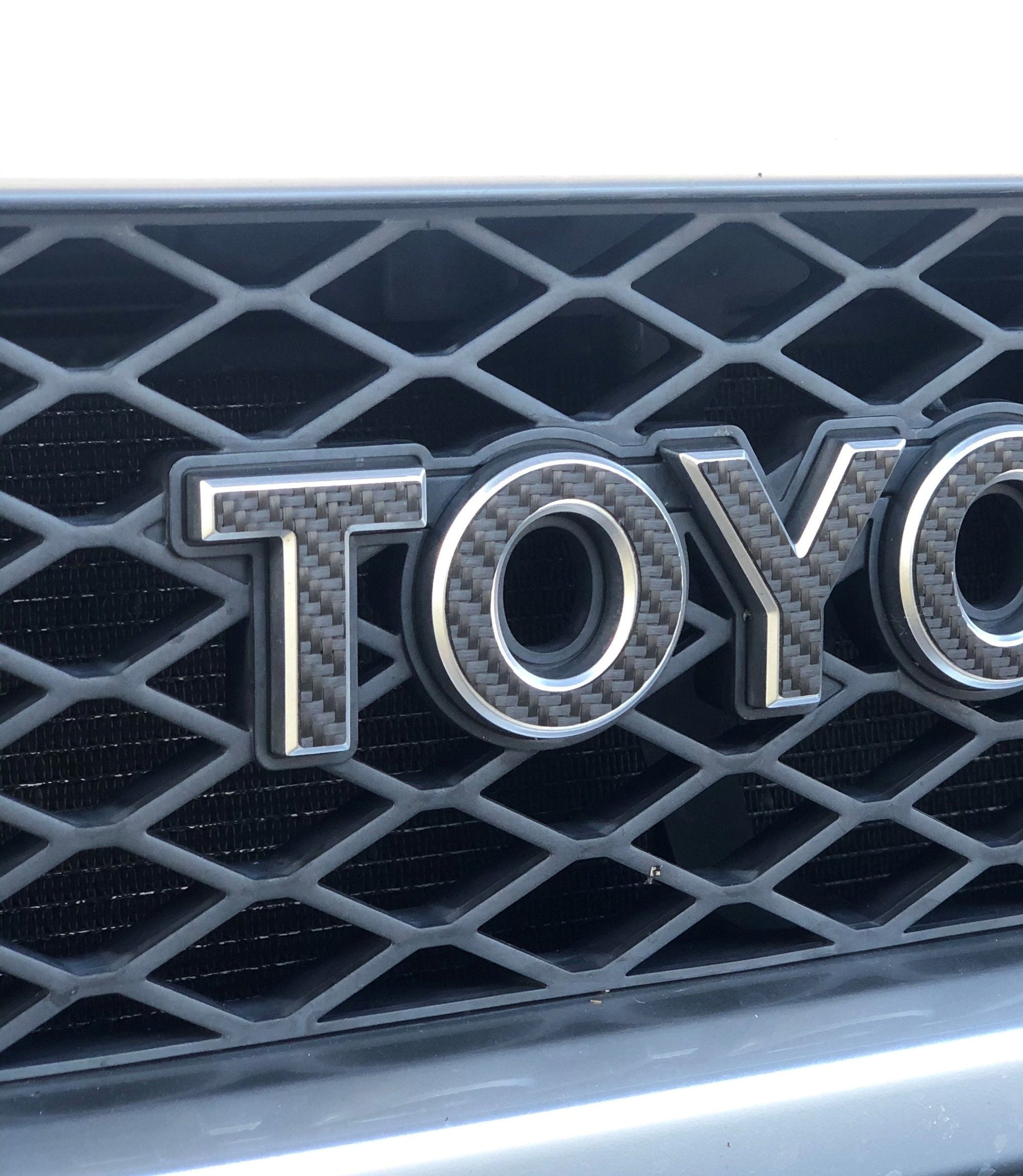 Close-up of a Toyota logo on a car grille with a black honeycomb pattern.